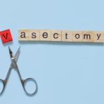 the word vasectomy made with wooden tiles on a blue background; V is red and scissors are under the word